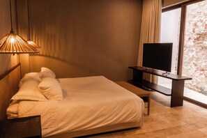 Een hotelkamer met een bed, een televisie op een standaard en een raam met uitzicht op een bakstenen muur.