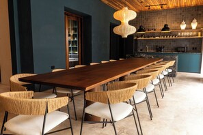 Een lange eettafel met rieten stoelen, een houten plafond en een keuken met planken.