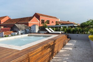 A rooftop swimming pool with wooden deck and lounge chairs, surrounded by buildings with red-tiled roofs. - Vrbo Property (Cartagena de Indias)