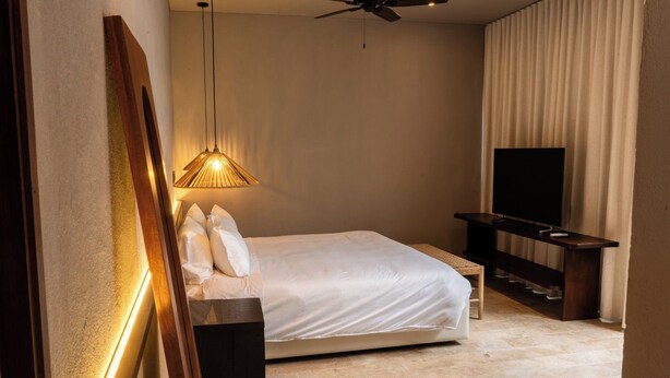Una habitación de hotel con una cama, un televisor, un ventilador de techo y una lámpara fijada a la pared.