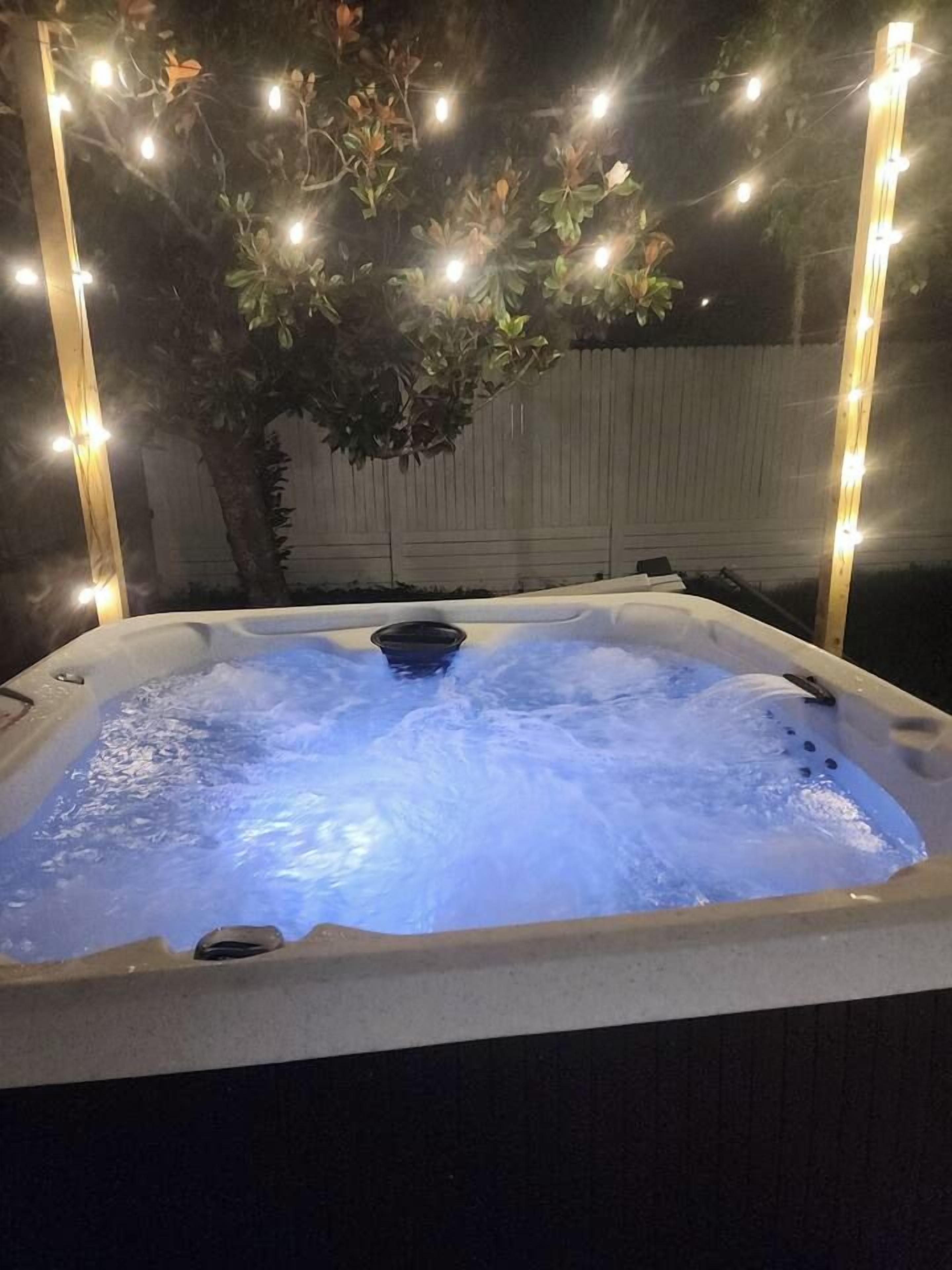 A hot tub with water jets, surrounded by string lights and a tree.