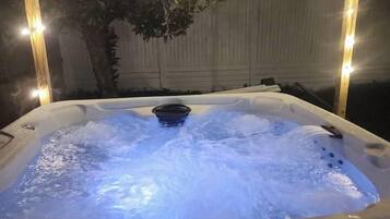 A hot tub with water jets, surrounded by string lights and a tree.