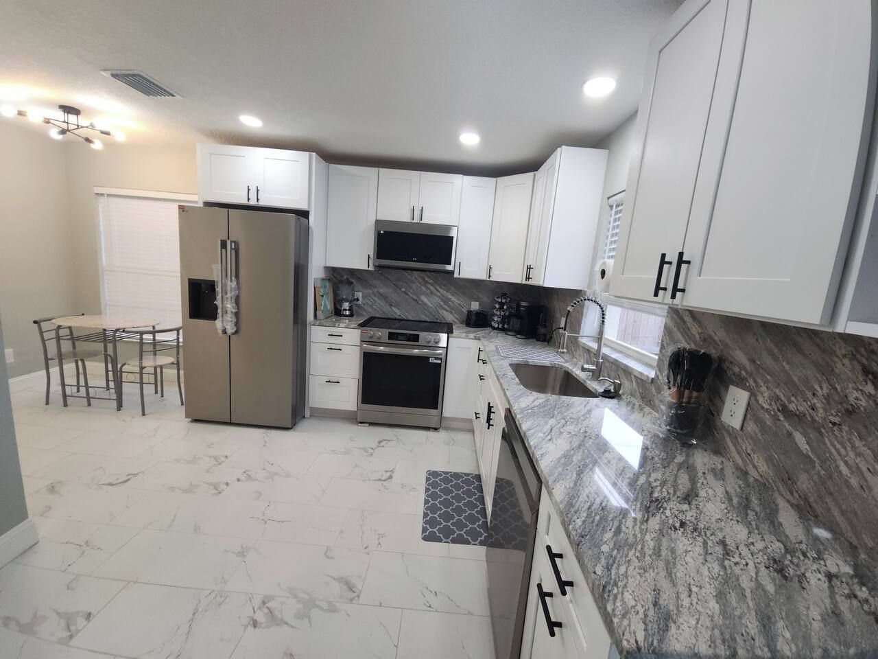 A modern kitchen with white cabinets, a stainless steel refrigerator, a built-in oven, and a granite countertop.