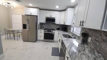 A modern kitchen with white cabinets, a stainless steel refrigerator, a built-in oven, and a granite countertop.