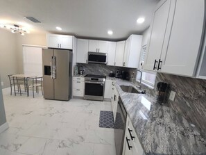 A modern kitchen with white cabinets, a stainless steel refrigerator, a built-in oven, and a granite countertop. - Modern Tampa Retreat Hot Tub  EV Charger Sleeps 8 (Tampa)