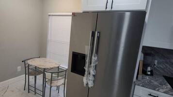 A compact kitchen with a stainless steel refrigerator, white cabinets, a small dining table with chairs, and a ceiling light fixture.