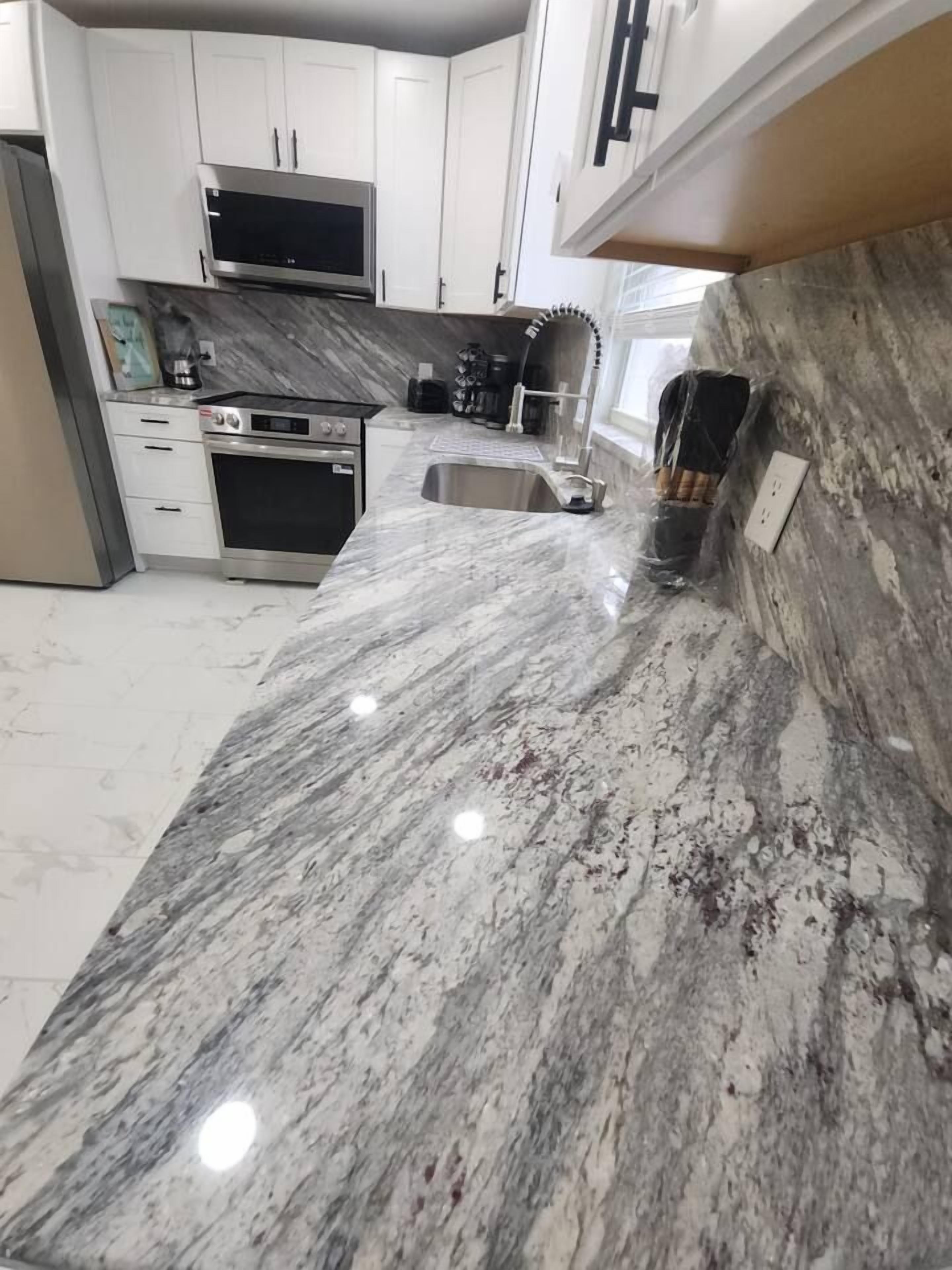 A kitchen with white cabinets, a stainless steel microwave, and a marble countertop.