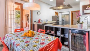 Cozinha moderna com área de refeições, com uma fruteira sobre a mesa, cafeteira e geladeira.