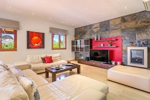 A modern living room with a stone accent wall, a flat-screen TV, and a sofa set. - Holiday Home 'Can Bou' with Sea View, Wi-Fi and Air Conditioning (Ses Salines)