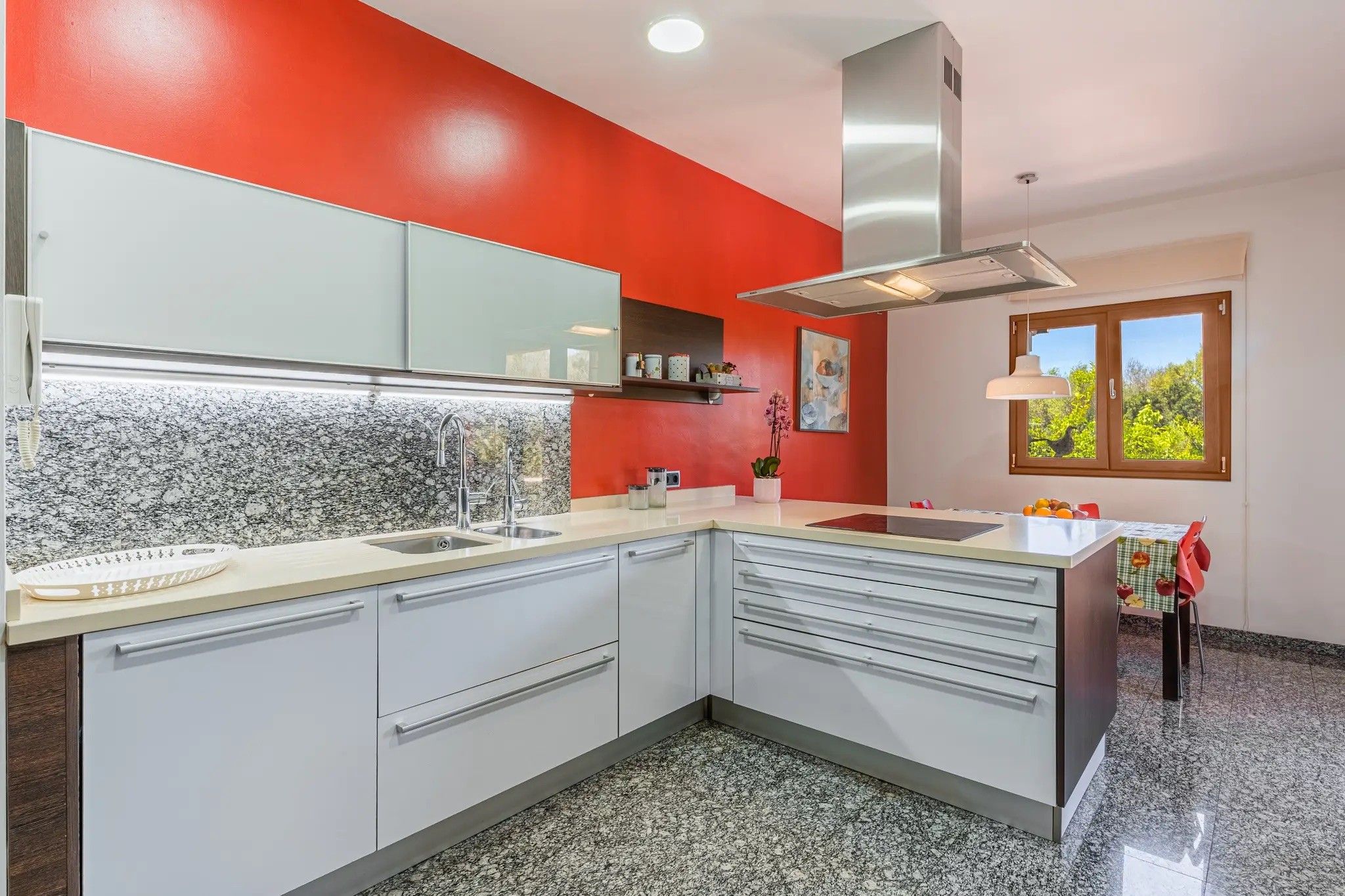 A modern kitchen with white cabinets, a granite countertop, a stainless steel range hood, and a window with a view of greenery.