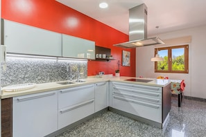 A modern kitchen with white cabinets, a granite countertop, a stainless steel range hood, and a window with a view of greenery. - Holiday Home 'Can Bou' with Sea View, Wi-Fi and Air Conditioning (Ses Salines)