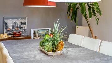 Een eettafel met een bloemstuk in het midden, een lijst met foto aan de muur en een lamp.