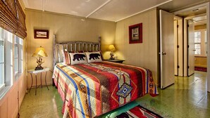 Een slaapkamer met een groot bed, twee bedlampen, een raam met zonwering en een deur die naar een andere kamer leidt.