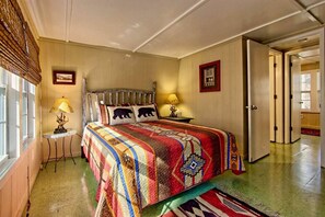 A bedroom with a large bed, two bedside lamps, a window with blinds, and a door leading to another room. - Cozy Mountain Cottage w/ Custom Laurel Furnishings — Pet Friendly, Sleeps 4 (Lakemont)