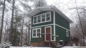 Een chalet met twee verdiepingen en een rode deur, omgeven door een besneeuwd bos.