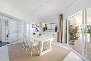 A modern kitchen with white cabinetry, a dining area with a white table and chairs, and a large sliding glass door leading to an outdoor patio. - Private villa with a large pool and guest house | Casa J&J | Andalusia (Alhaurín el Grande)