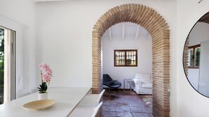 Un interior moderno con una pared blanca, un arco de ladrillo, un lavamanos blanco, una orquídea en maceta, una silla azul y un sofá blanco.