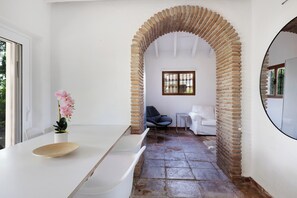 A modern interior with a white wall, a brick archway, a white sink, a potted orchid, a blue chair, and a white sofa. - Private villa with a large pool and guest house | Casa J&J | Andalusia (Alhaurín el Grande)