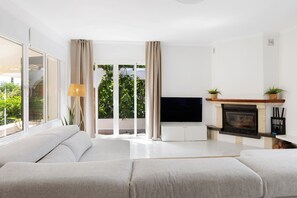A modern living room with a sofa, TV, fireplace, and large windows with curtains. - Private villa with a large pool and guest house | Casa J&J | Andalusia (Alhaurín el Grande)