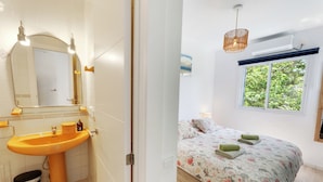 Baño con lavamanos, espejo y ventana. La habitación tiene una cama con ropa de cama floral y vista a zonas verdes.