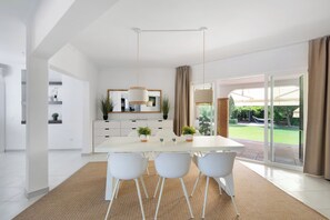 A modern kitchen with white cabinetry, a dining table with four chairs, and a view of the outdoor garden through large sliding glass doors. - Private villa with a large pool and guest house | Casa J&J | Andalusia (Alhaurín el Grande)