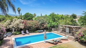 A rectangular swimming pool with a tiled deck, surrounded by lush greenery and flowering plants. - Private villa with a large pool and guest house | Casa J&J | Andalusia (Alhaurín el Grande)