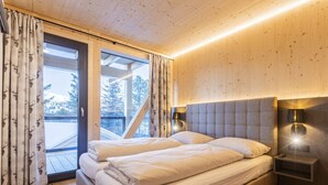 A bedroom with a large bed, a wooden ceiling, and a view of trees through a window. - Superior Chalet # 9 With Sauna & Hot Tub (Stadl-Predlitz)
