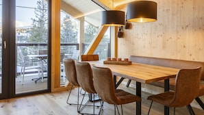 A modern interior with a wooden dining table, cushioned chairs, and a large window overlooking a deck. - Superior Chalet # 9 With Sauna & Hot Tub (Stadl-Predlitz)