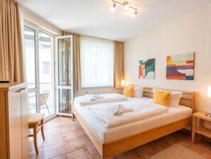 A hotel room with a large bed, a desk, a chair, and a view through a glass door. - Apartment Building Linquenda 09 (Heringsdorf)