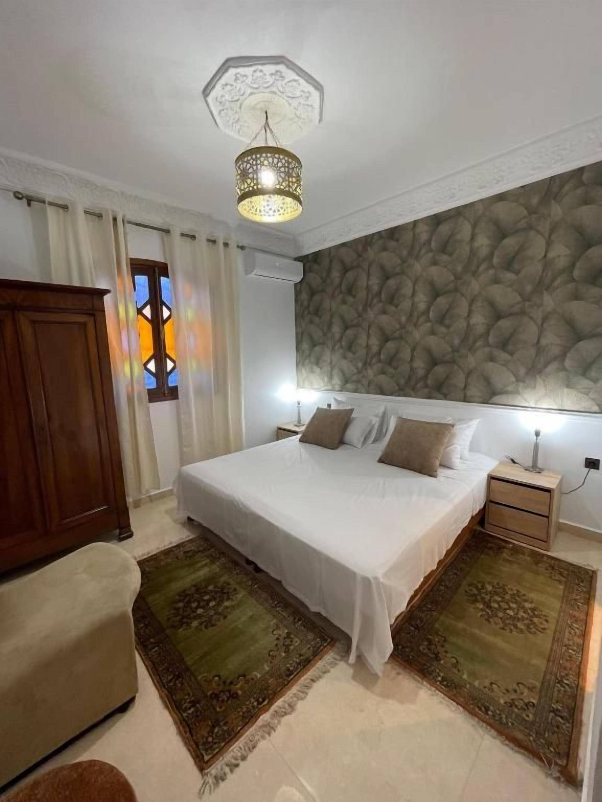 A bedroom with a large bed, a nightstand, a wooden wardrobe, and a decorative ceiling light.