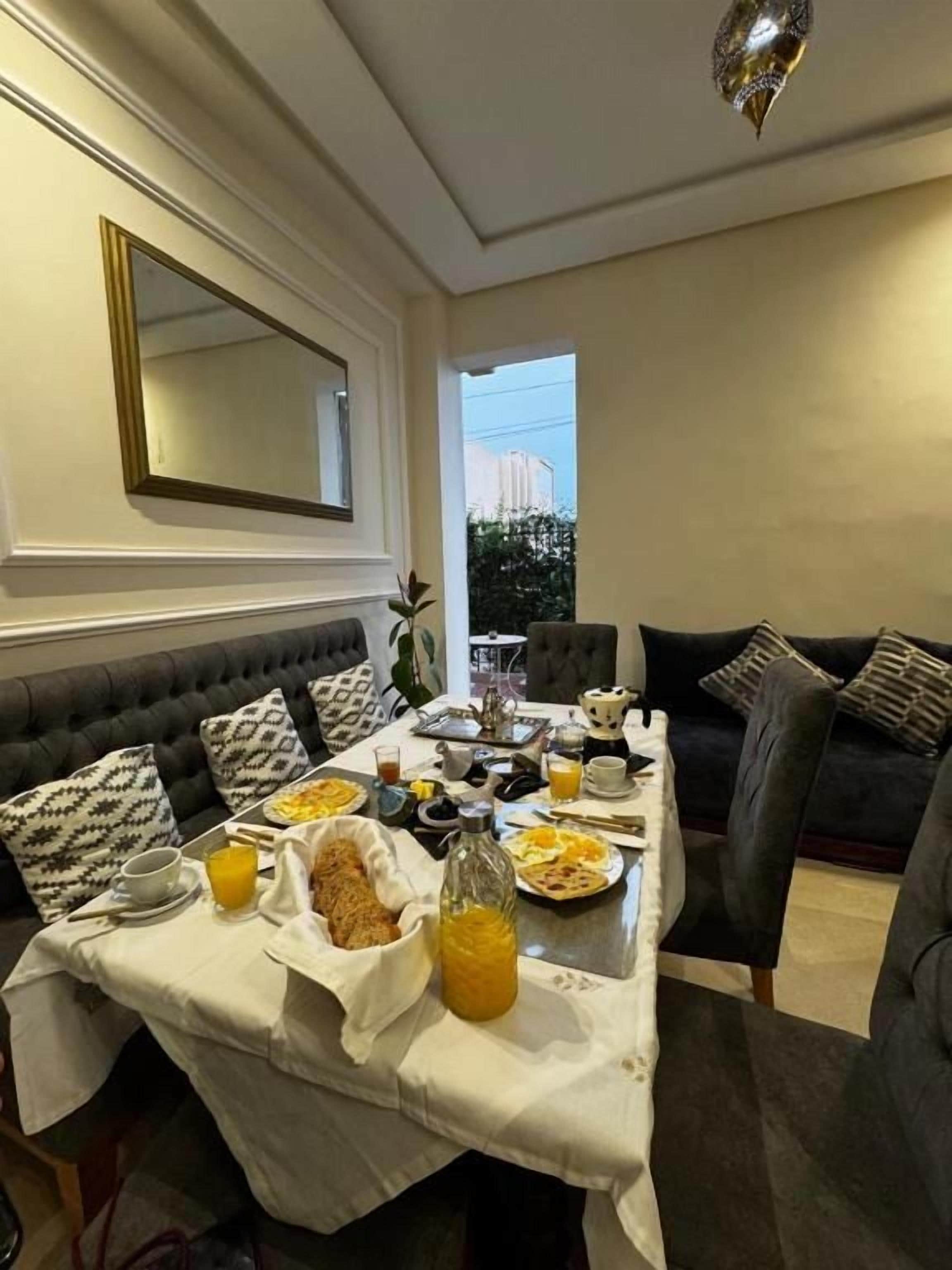 Un comedor con una mesa lista para el desayuno, un sofá y un espejo grande en la pared.