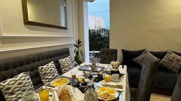 Un comedor con una mesa lista para el desayuno, un sofá y un espejo grande en la pared.