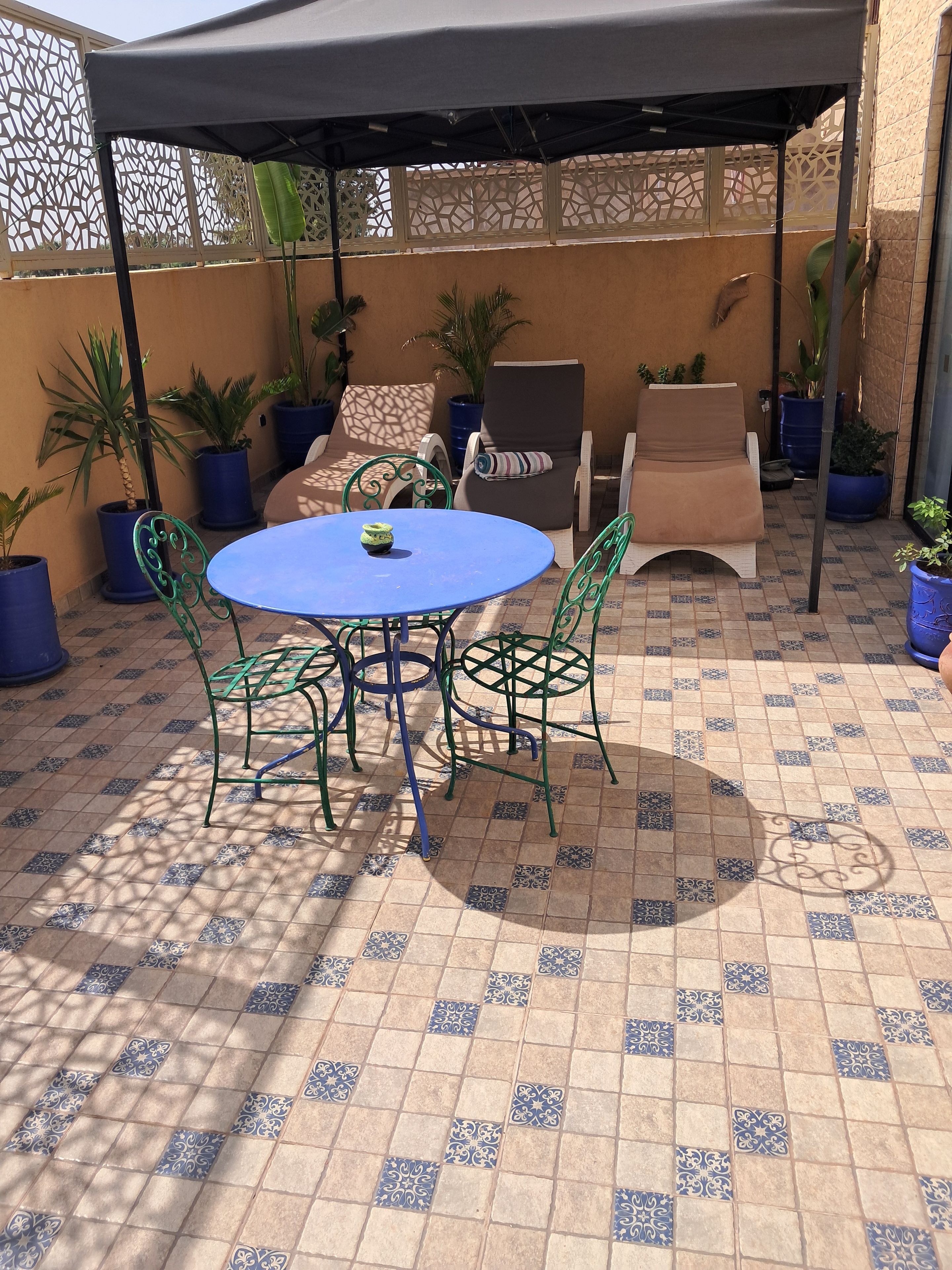 Un patio couvert avec une table ronde et des chaises, des plantes en pot et un sol à motifs.