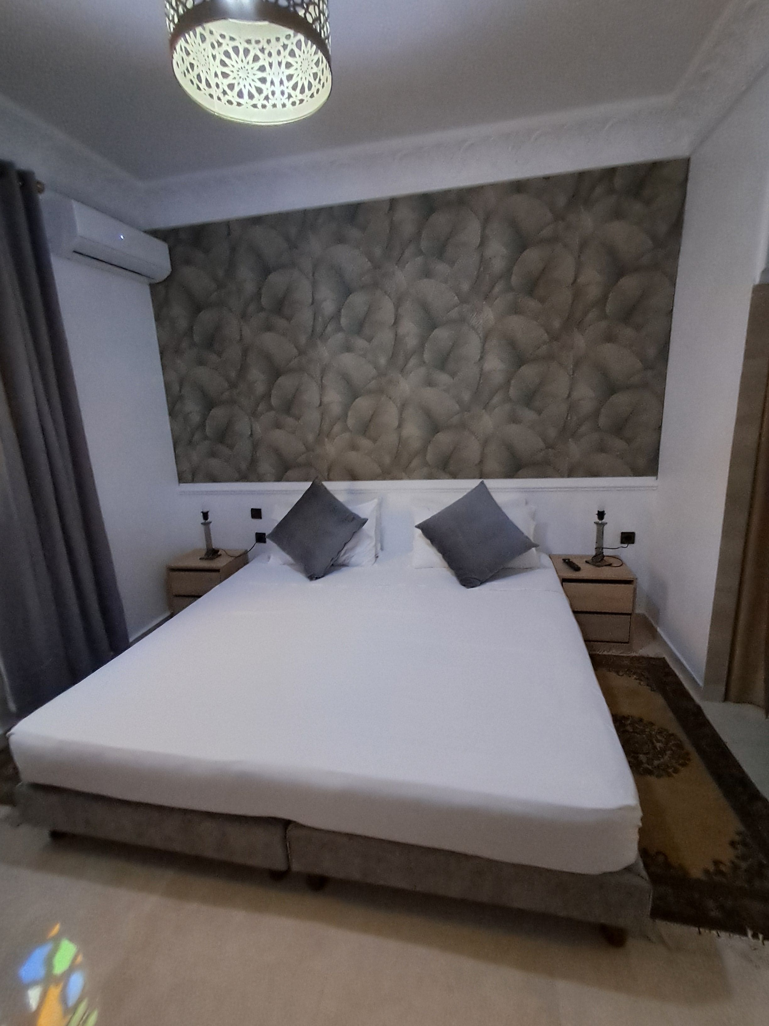 Un dormitorio con una cama grande, dos mesitas de noche, una lámpara de pared y una pared con textura.