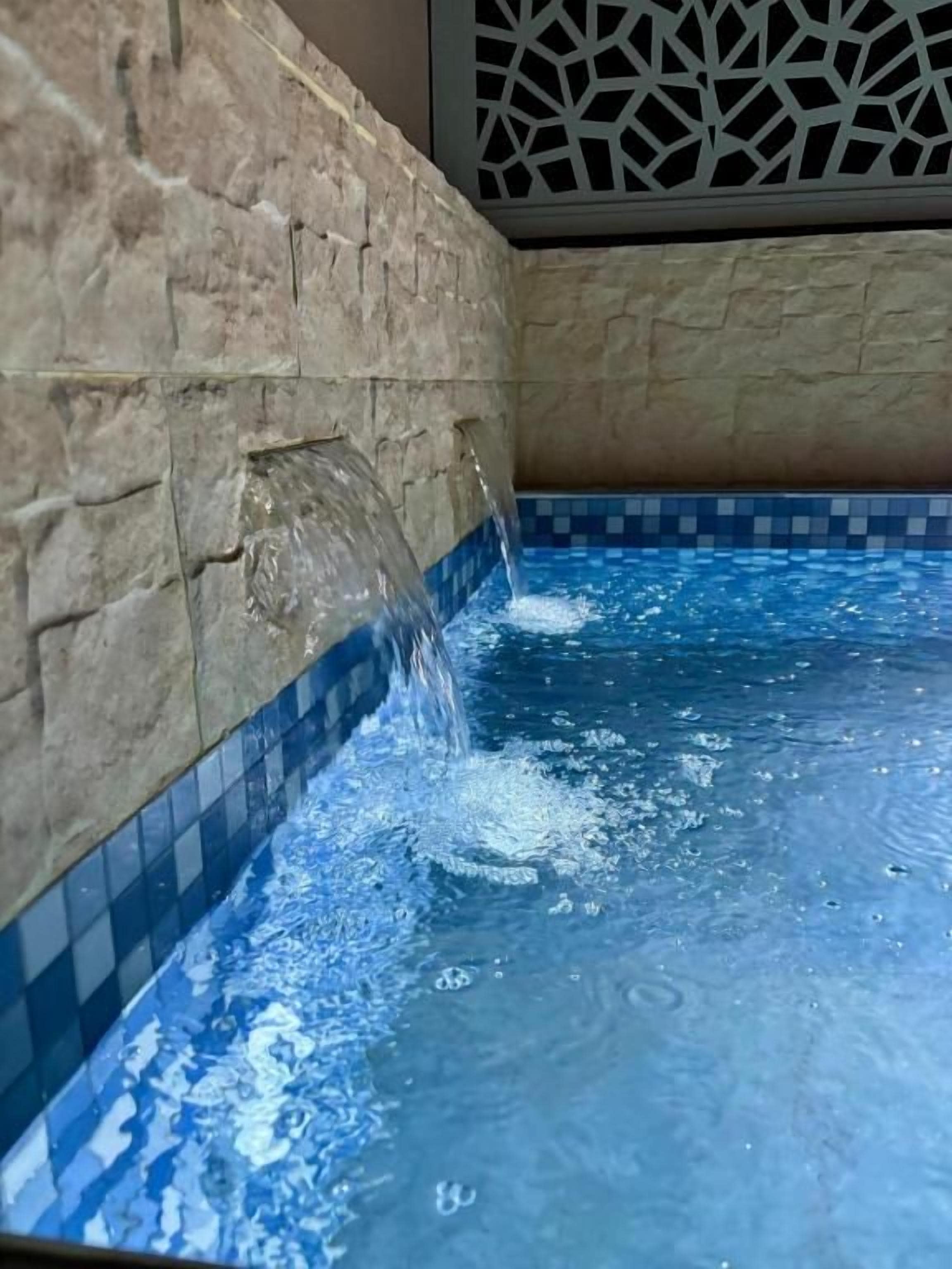 Una piscina con agua cristalina, una pared de piedra y un borde de azulejos.