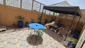 An outdoor patio with a blue table and chairs, potted plants, and a covered area with lounge chairs.