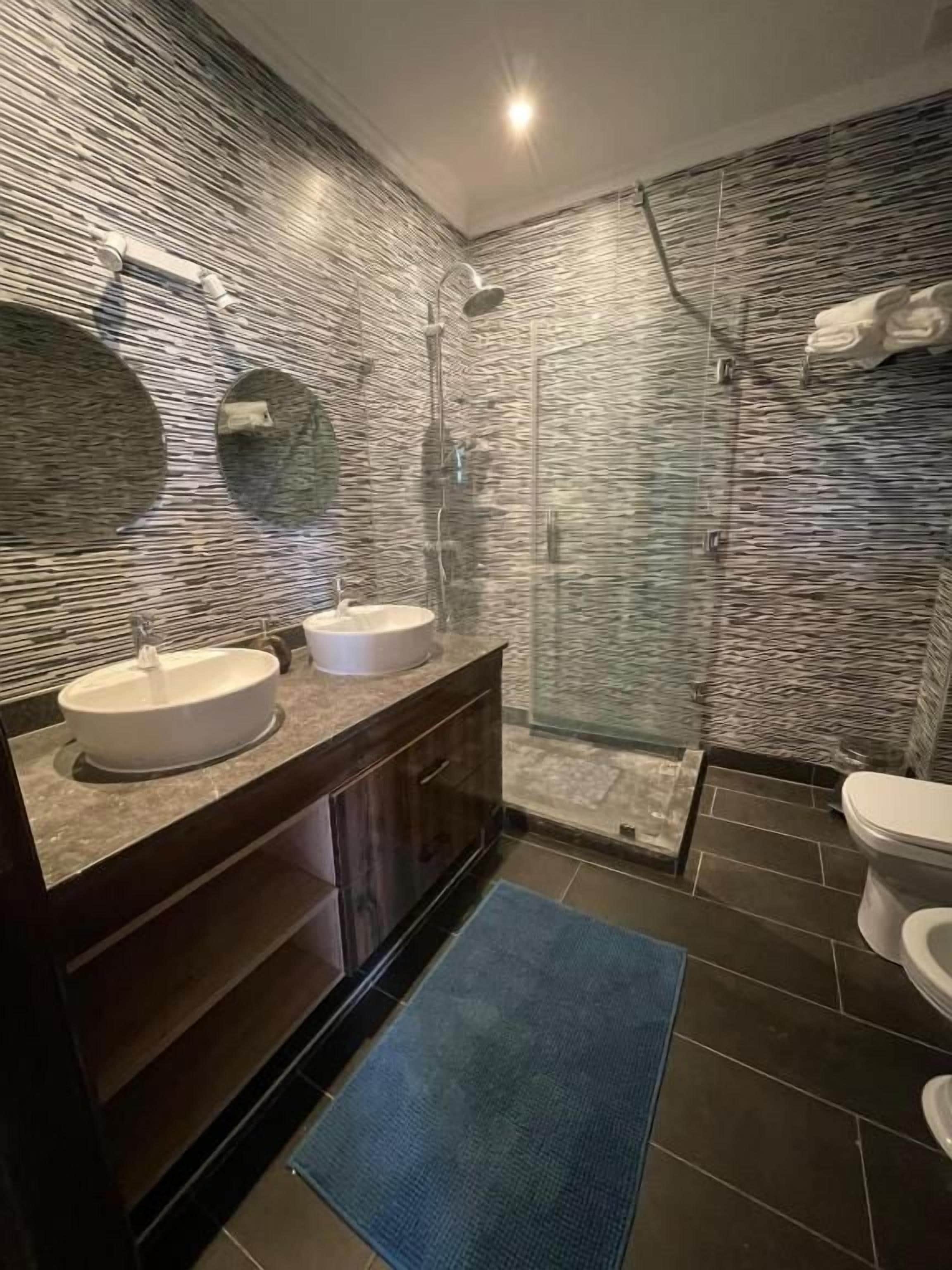 Un baño con diseño moderno, que incluye un mueble lavamanos doble, cabina de ducha con mampara de vidrio y un inodoro.
