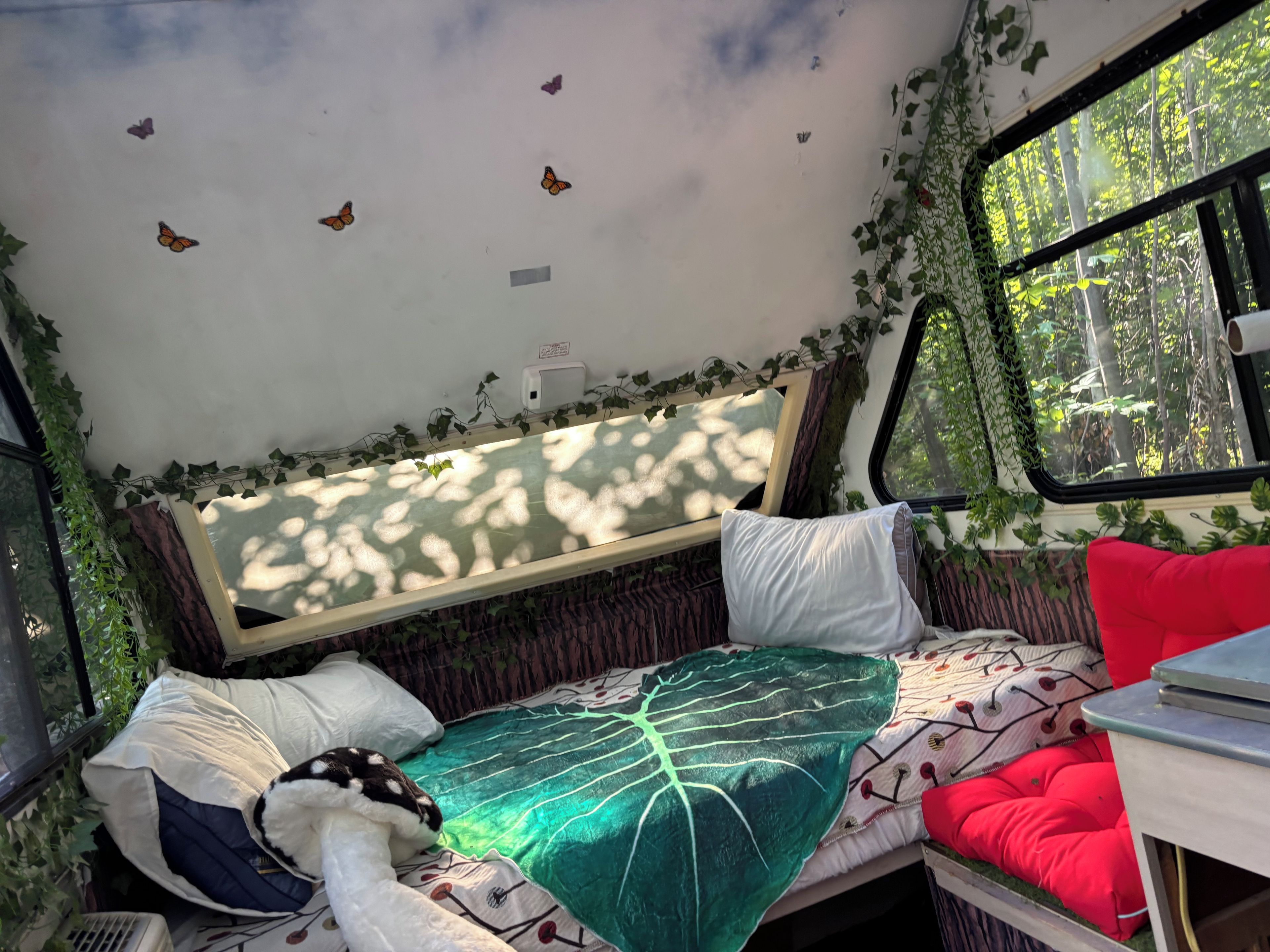 Un intérieur chaleureux avec un lit, des oreillers et une fenêtre donnant sur les arbres.