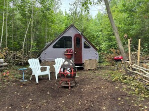 A small cabin with a porch, surrounded by trees and a red vehicle.