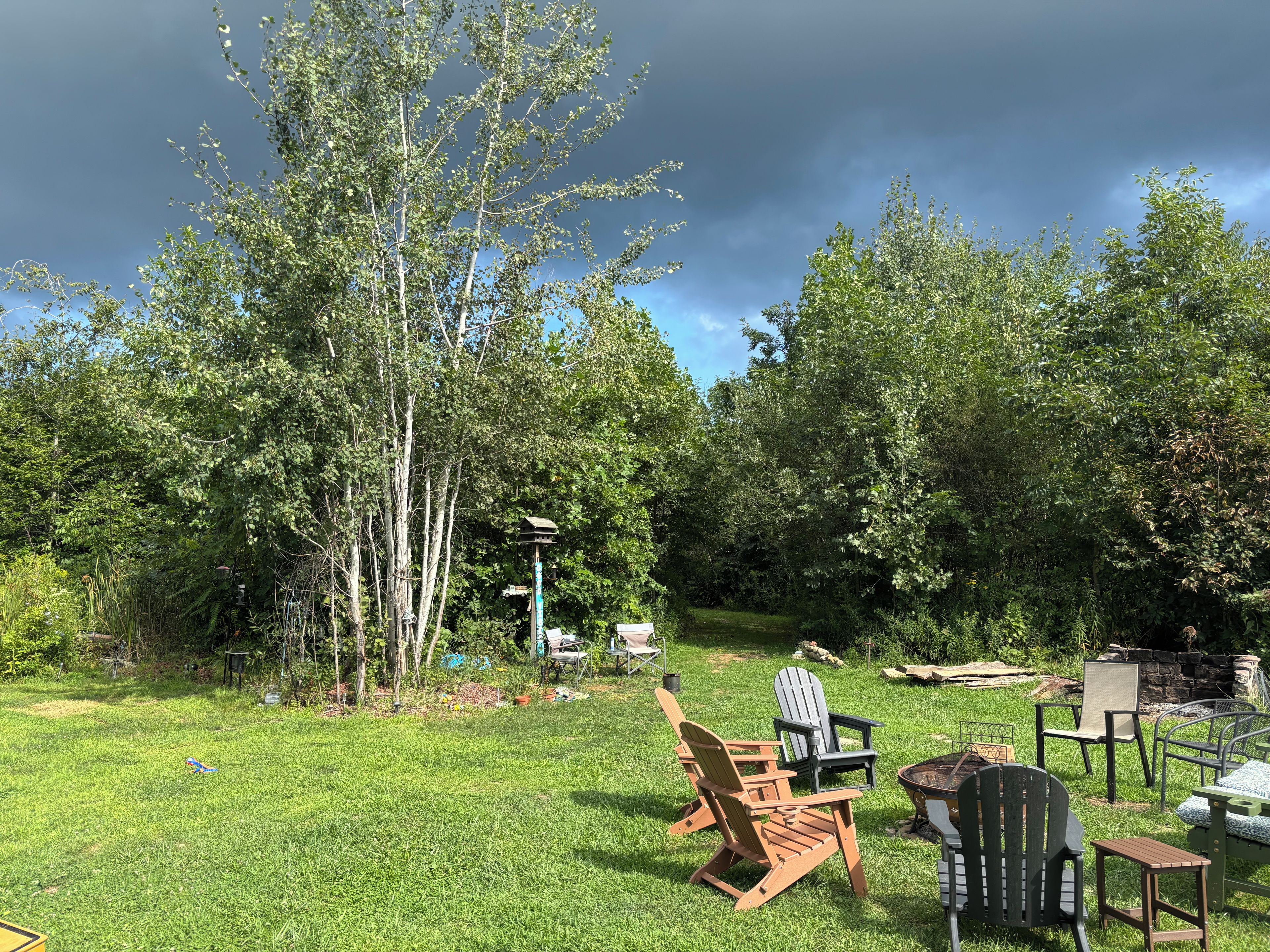 A grassy backyard with Adirondack chairs and a fire pit.