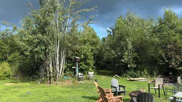 A grassy backyard with Adirondack chairs and a fire pit.