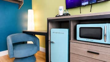 Ein Zimmer mit blauem Sessel, einer Kühl-Gefrier-Kombination im Vintage-Stil und einem Fernseher, der verschiedene Streaming-Dienste anzeigt.