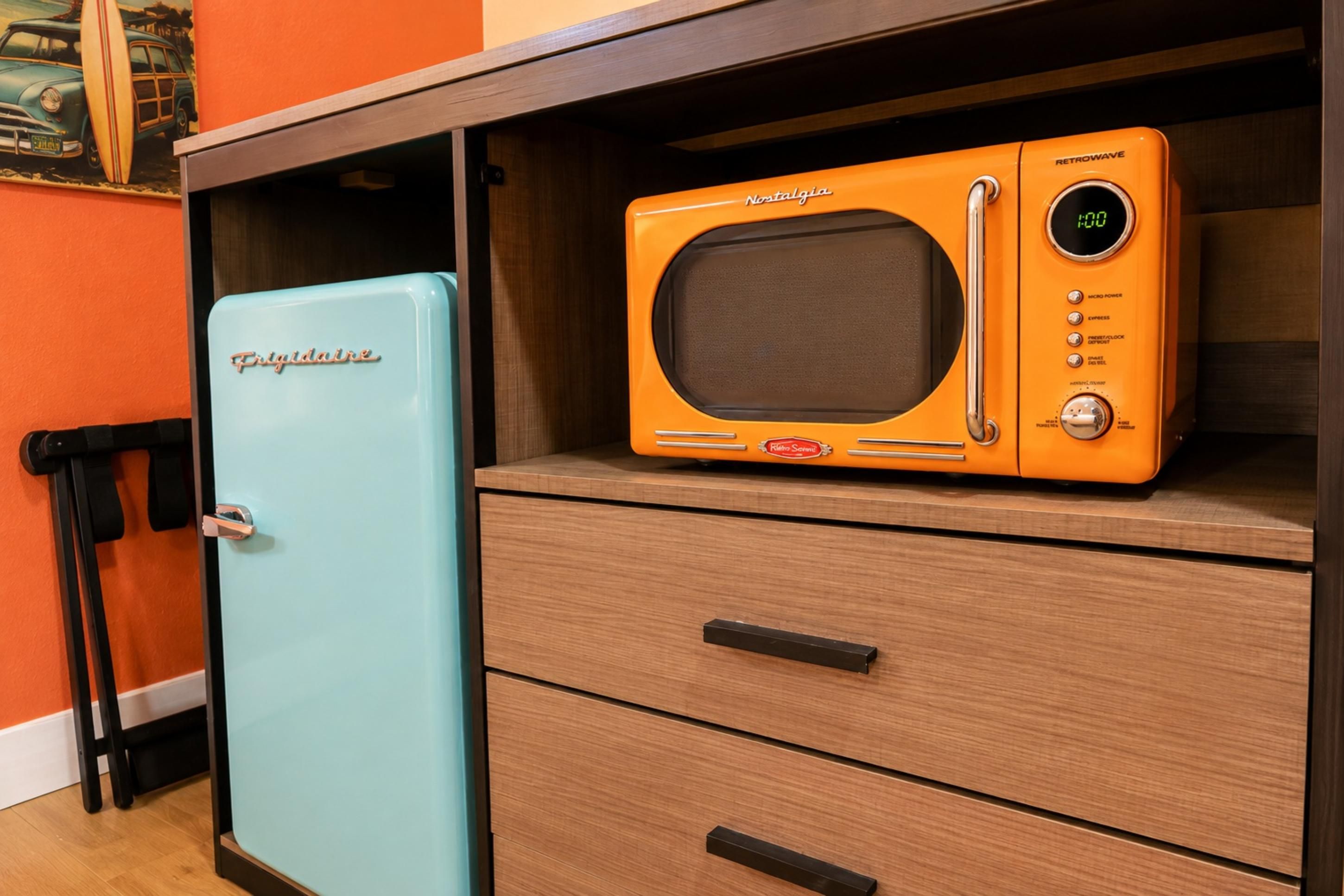 A retro-style kitchen with a vintage orange microwave on top of a wooden cabinet, a light blue refrigerator, and a wooden drawer unit.