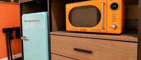 A retro-style kitchen with a vintage orange microwave on top of a wooden cabinet, a light blue refrigerator, and a wooden drawer unit.