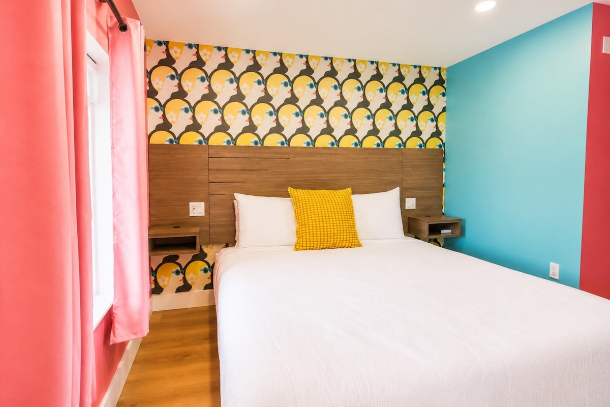 A hotel room with a bed, a nightstand, a wooden headboard, a patterned wallpaper, and a red wall.