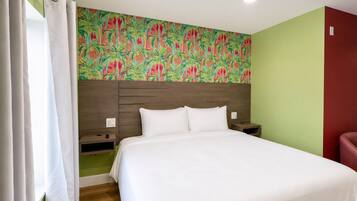Quarto de hotel com cama, mesa de cabeceira, televisão na parede e uma parede de destaque vermelha.