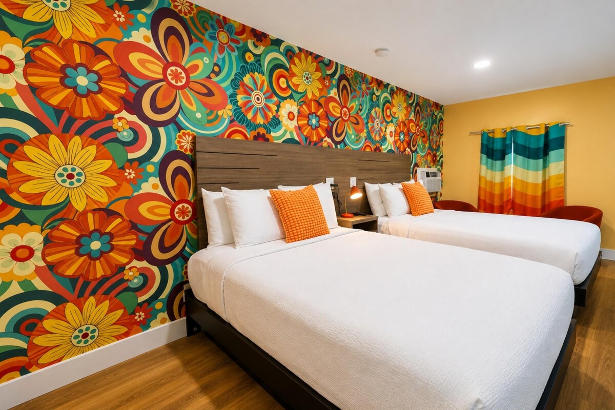 A hotel room with two beds, a colorful floral wall mural, a wooden headboard, and a striped curtain.