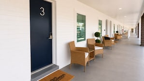 A hotel corridor with numbered doors, wicker chairs, and a doormat with text. - The Blu - A Boutique Motel (Port St. Joe)