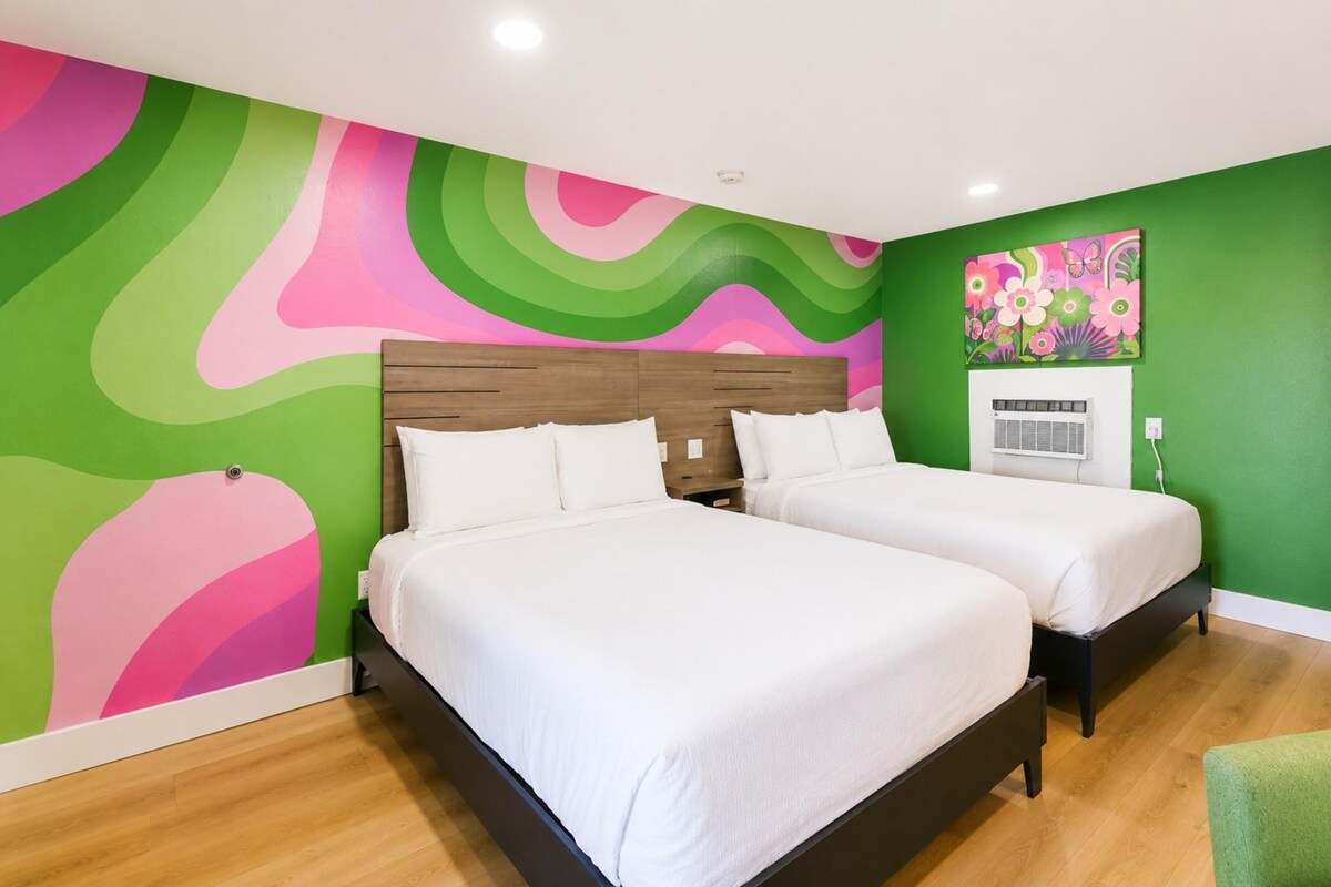 A room with two beds, a green wall, and a colorful abstract mural.