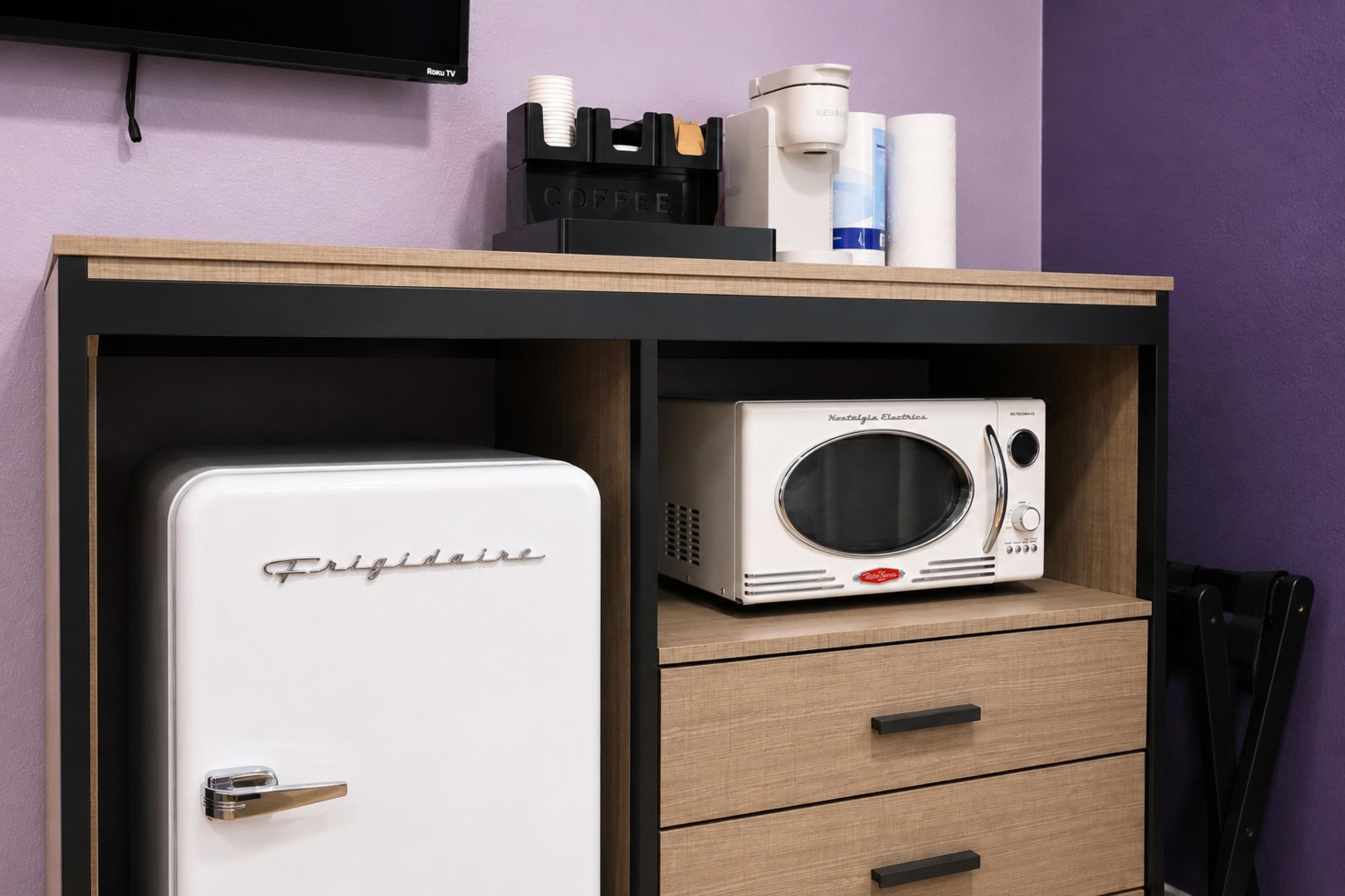 A compact kitchenette with a white refrigerator, a microwave, and a coffee maker on a wooden countertop.